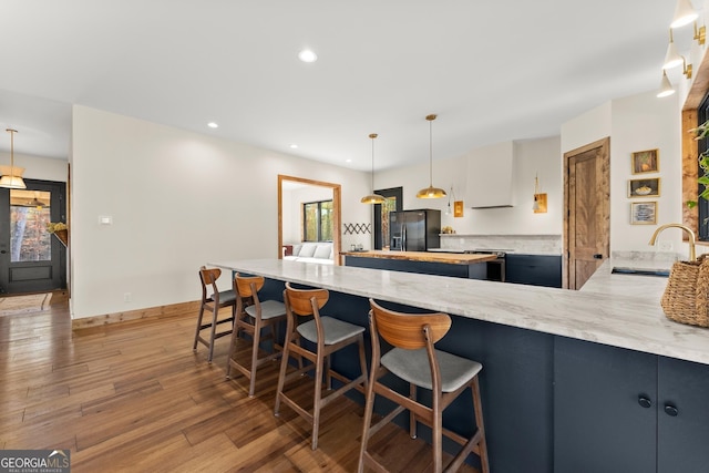 kitchen with decorative light fixtures, sink, black fridge, kitchen peninsula, and hardwood / wood-style flooring