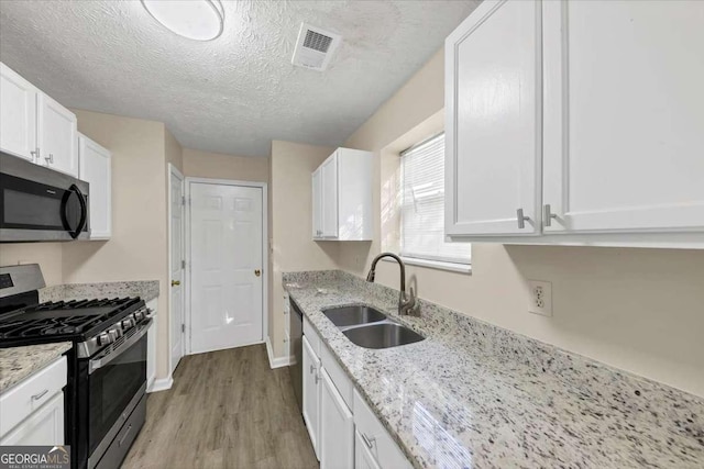 kitchen with light stone countertops, sink, stainless steel appliances, light hardwood / wood-style flooring, and white cabinets