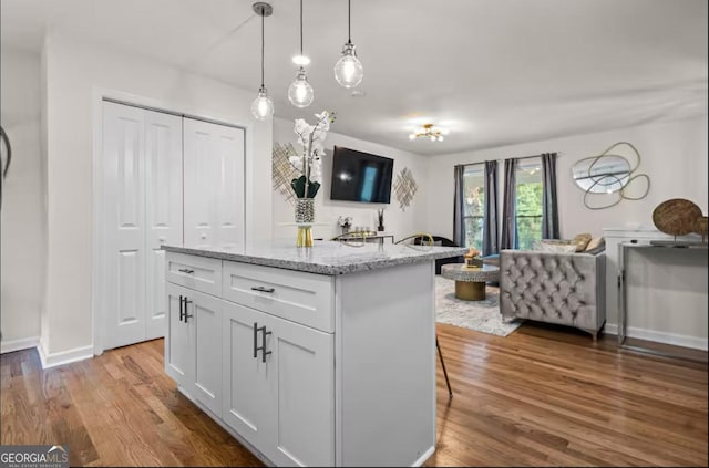 kitchen with a center island, white cabinets, light stone countertops, decorative light fixtures, and wood-type flooring