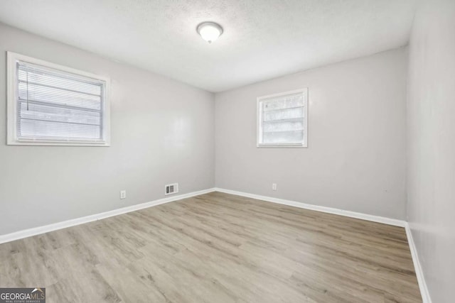 empty room with a textured ceiling and light hardwood / wood-style flooring