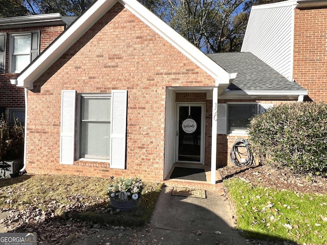 doorway to property featuring a shingled roof and brick siding