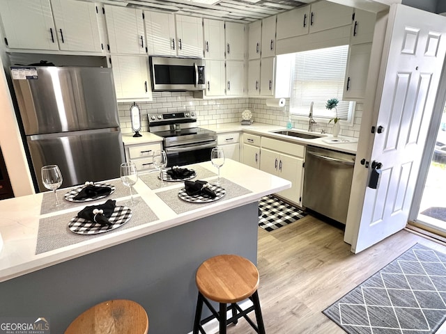 kitchen with stainless steel appliances, tasteful backsplash, light countertops, light wood-style floors, and a sink