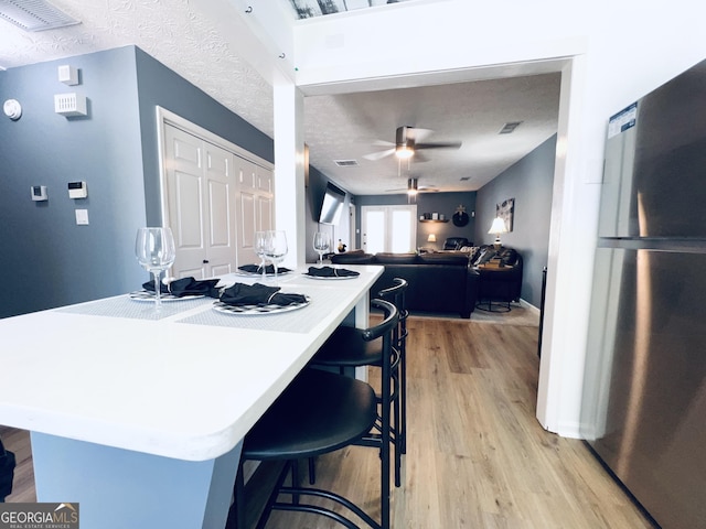 kitchen featuring a ceiling fan, light wood-style flooring, a breakfast bar area, freestanding refrigerator, and a textured ceiling