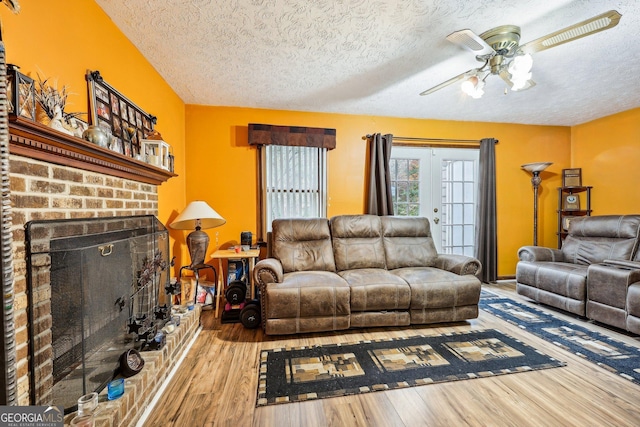 living room with ceiling fan, a fireplace, wood-type flooring, and a textured ceiling