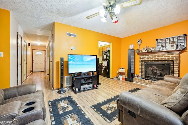 living room featuring a fireplace, a textured ceiling, light hardwood / wood-style flooring, and ceiling fan