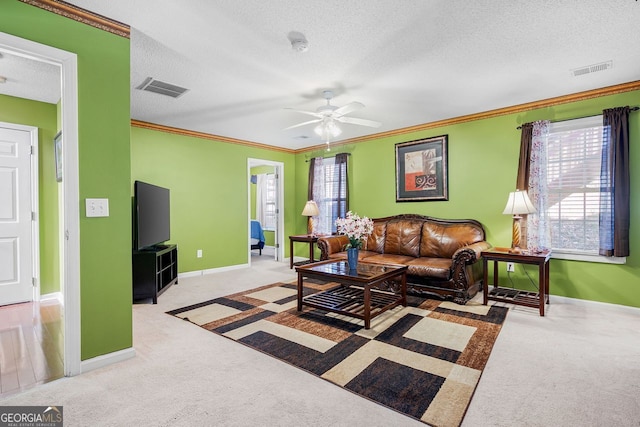 living room featuring ceiling fan, light colored carpet, ornamental molding, and a textured ceiling