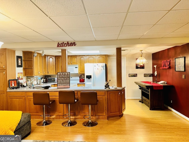 kitchen with a kitchen breakfast bar, a paneled ceiling, white appliances, sink, and light hardwood / wood-style floors