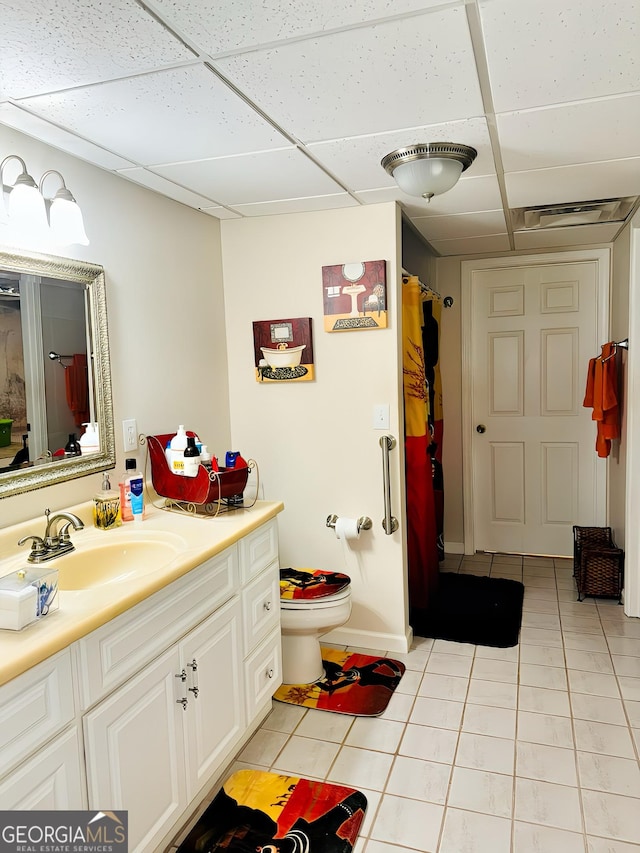 bathroom with tile patterned floors, a drop ceiling, vanity, and toilet