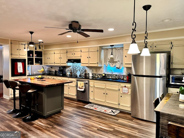 kitchen featuring appliances with stainless steel finishes, dark hardwood / wood-style flooring, sink, cream cabinets, and pendant lighting