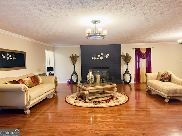 living room featuring an inviting chandelier, crown molding, a brick fireplace, hardwood / wood-style flooring, and a textured ceiling