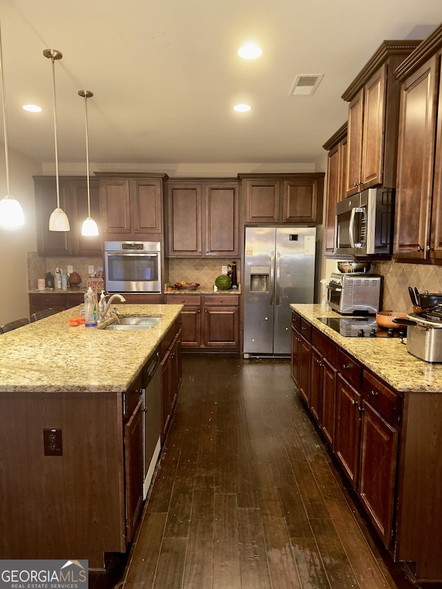 kitchen featuring dark hardwood / wood-style flooring, backsplash, stainless steel appliances, pendant lighting, and an island with sink