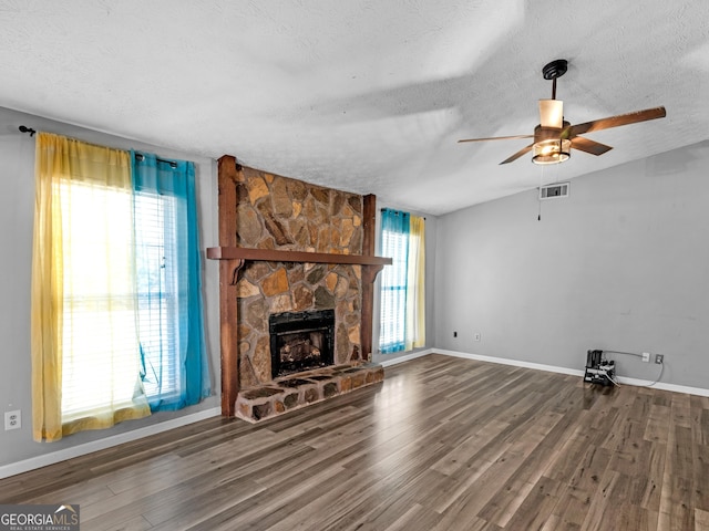 unfurnished living room featuring ceiling fan, a stone fireplace, dark hardwood / wood-style flooring, and a textured ceiling