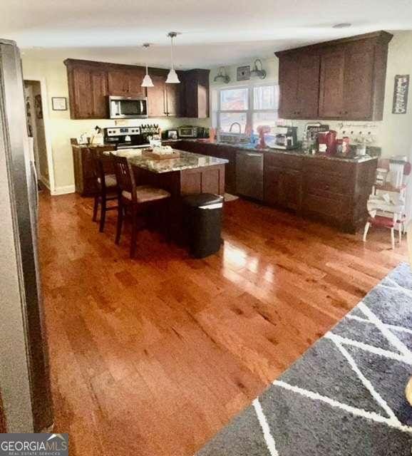 kitchen with a center island, appliances with stainless steel finishes, dark brown cabinets, dark hardwood / wood-style flooring, and a breakfast bar area