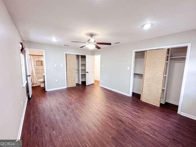 unfurnished bedroom featuring ceiling fan, dark hardwood / wood-style floors, and connected bathroom