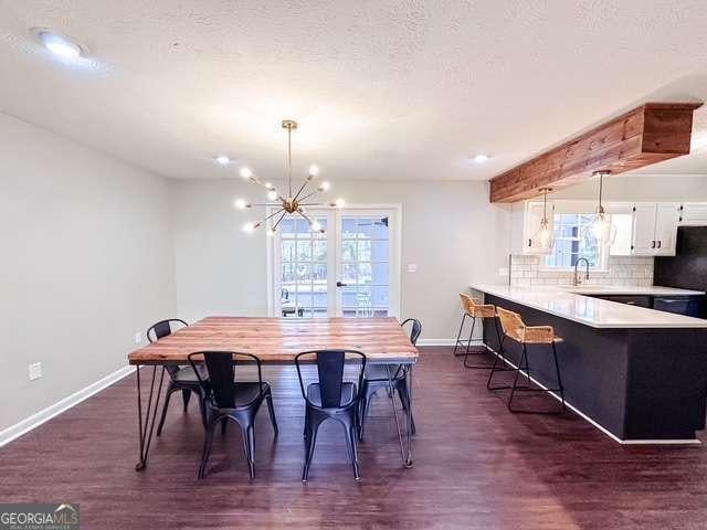 dining room with sink, dark wood-type flooring, a textured ceiling, and an inviting chandelier