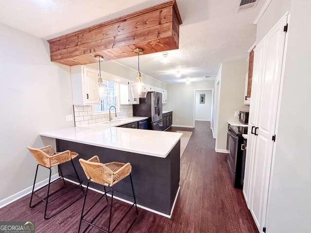 kitchen with kitchen peninsula, electric range, a breakfast bar area, white cabinetry, and stainless steel refrigerator