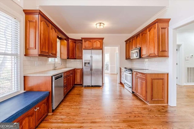 kitchen with light wood-type flooring, stainless steel appliances, and crown molding