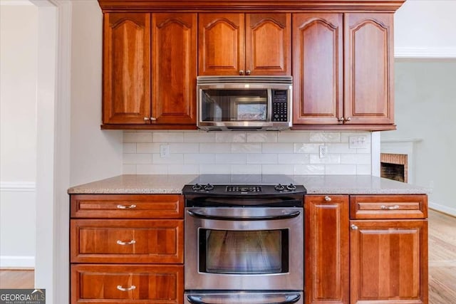 kitchen with light stone countertops, stainless steel appliances, tasteful backsplash, crown molding, and light hardwood / wood-style floors