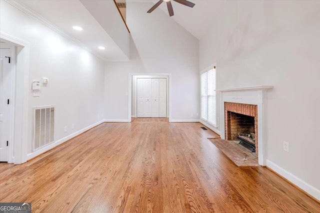 unfurnished living room with high vaulted ceiling, ceiling fan, light wood-type flooring, a fireplace, and ornamental molding