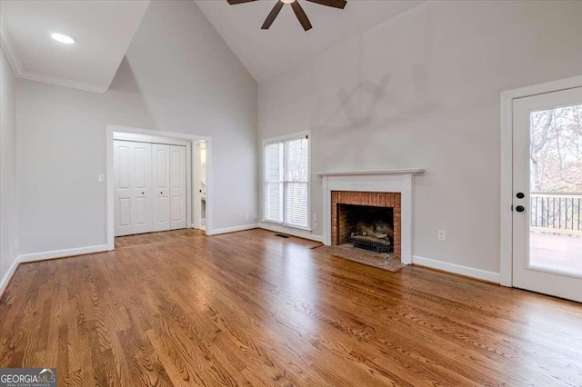 unfurnished living room with wood-type flooring, high vaulted ceiling, ceiling fan, and a brick fireplace