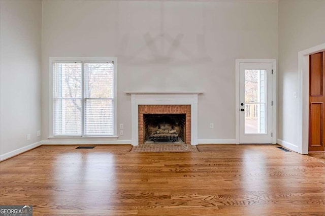 unfurnished living room with a high ceiling, hardwood / wood-style flooring, a brick fireplace, and plenty of natural light