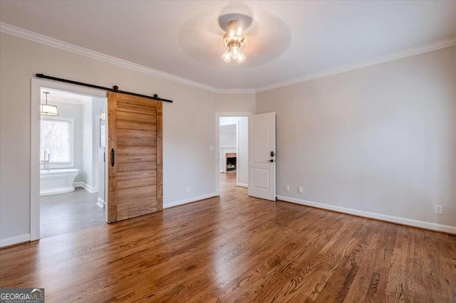 unfurnished room featuring a barn door, crown molding, ceiling fan, and hardwood / wood-style flooring