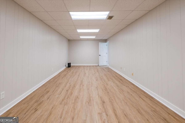 basement with a paneled ceiling, wood walls, and light wood-type flooring