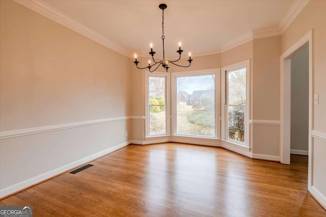 unfurnished dining area with hardwood / wood-style floors, a healthy amount of sunlight, ornamental molding, and an inviting chandelier