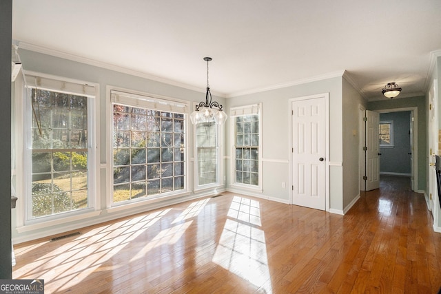 unfurnished dining area with hardwood / wood-style flooring, ornamental molding, and an inviting chandelier