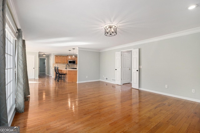 unfurnished living room featuring crown molding, light hardwood / wood-style flooring, and an inviting chandelier