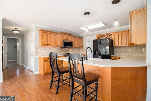 kitchen featuring a kitchen breakfast bar, black fridge, crown molding, and decorative light fixtures