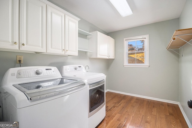 clothes washing area with washer and clothes dryer, cabinets, and light wood-type flooring