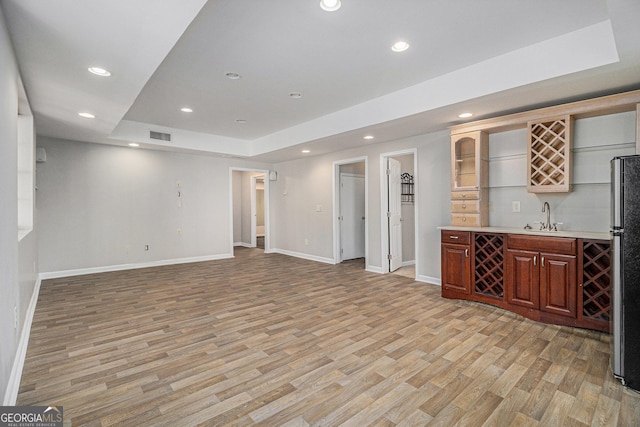 unfurnished living room with indoor wet bar, light hardwood / wood-style flooring, and a tray ceiling