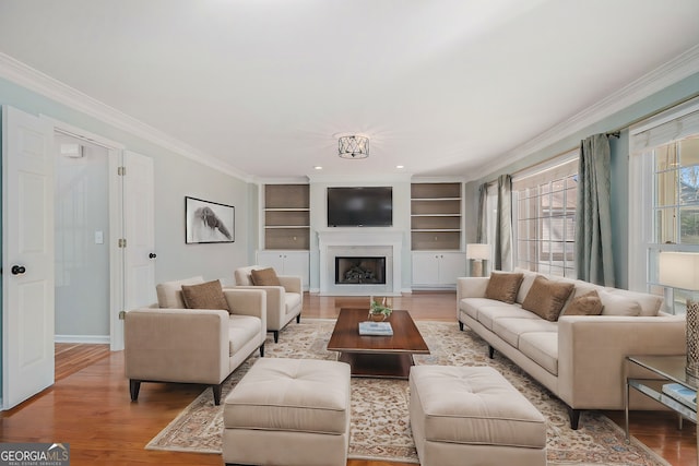 living room with built in shelves, a premium fireplace, ornamental molding, and wood-type flooring