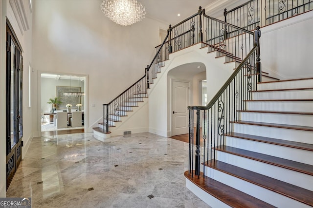 foyer with crown molding, a chandelier, and a high ceiling