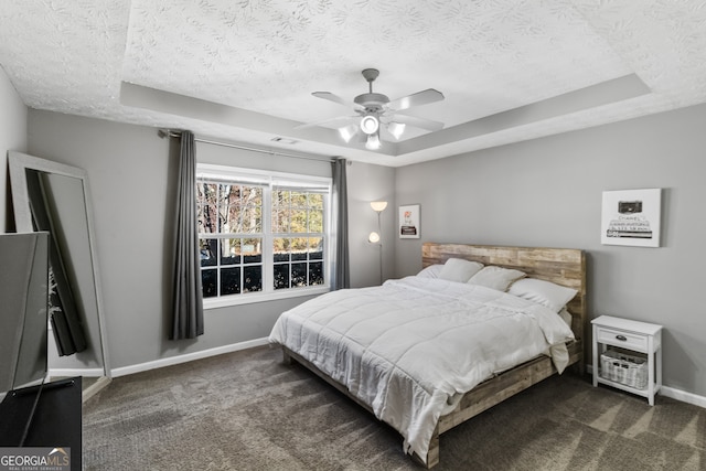 carpeted bedroom with a tray ceiling, ceiling fan, and a textured ceiling