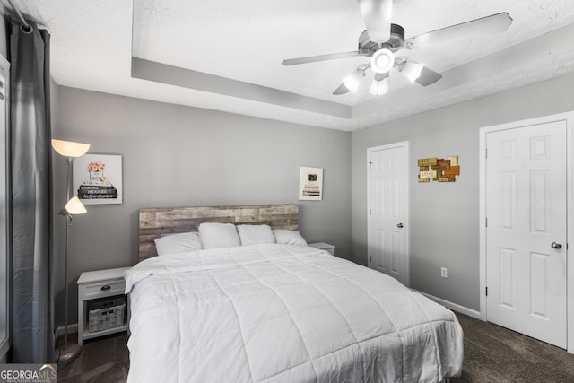 carpeted bedroom featuring a textured ceiling, a tray ceiling, and ceiling fan