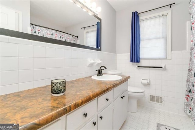 bathroom with tile patterned flooring, toilet, a wealth of natural light, and tile walls