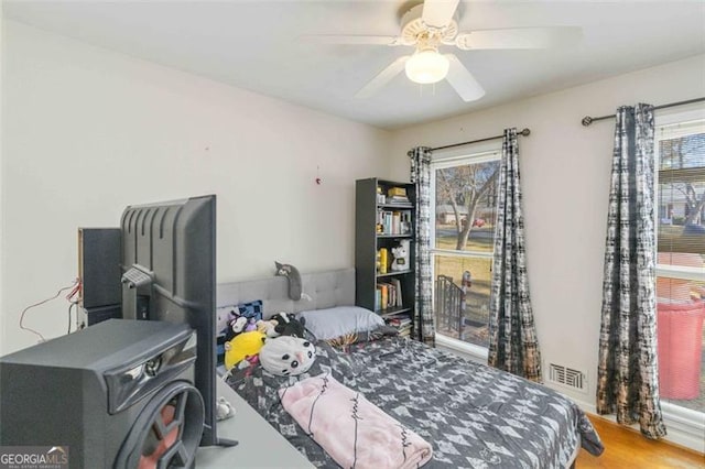 bedroom featuring hardwood / wood-style floors, a wood stove, and ceiling fan