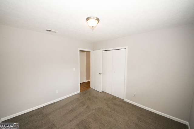 unfurnished bedroom featuring dark carpet and a closet