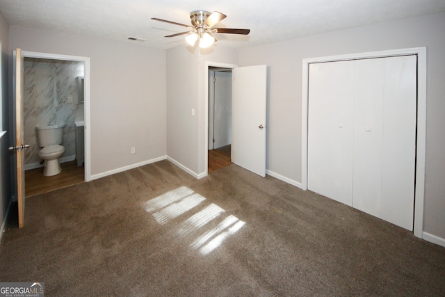 unfurnished bedroom with dark colored carpet, ceiling fan, a closet, and ensuite bath