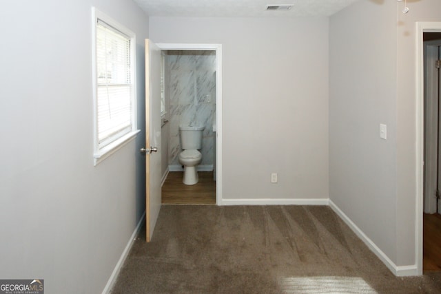 bedroom featuring dark colored carpet, a textured ceiling, and connected bathroom