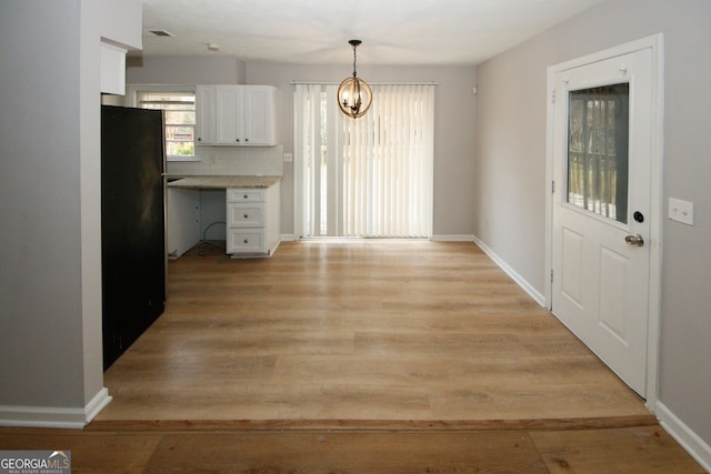 kitchen featuring backsplash, black fridge, light hardwood / wood-style floors, white cabinetry, and hanging light fixtures