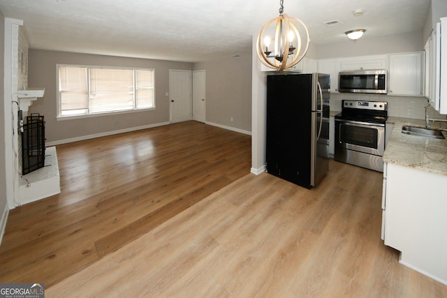 kitchen featuring white cabinetry, sink, hanging light fixtures, light hardwood / wood-style floors, and appliances with stainless steel finishes