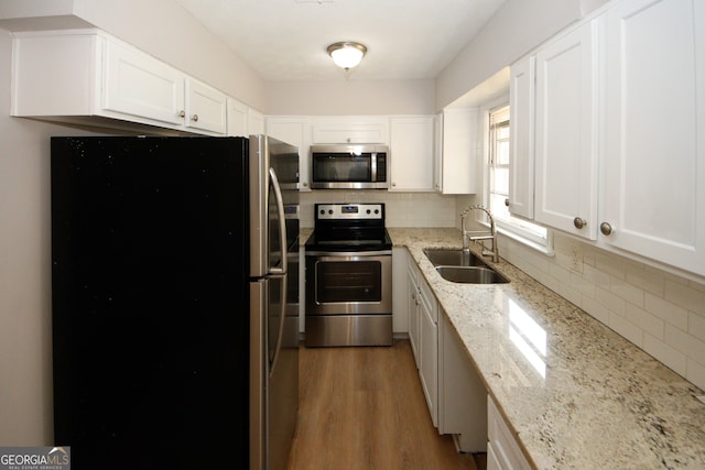 kitchen with light stone countertops, sink, stainless steel appliances, light hardwood / wood-style floors, and white cabinets