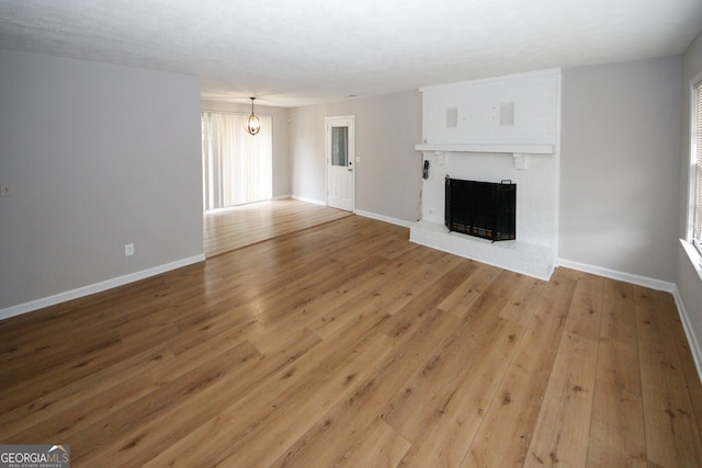 unfurnished living room featuring hardwood / wood-style floors, an inviting chandelier, and a brick fireplace