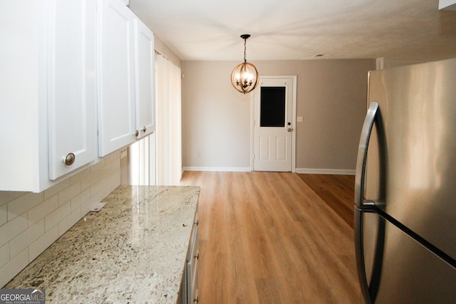 kitchen featuring white cabinetry, light stone countertops, stainless steel fridge, light hardwood / wood-style floors, and decorative backsplash