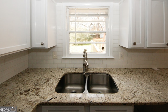 details with white cabinets, decorative backsplash, light stone countertops, and sink