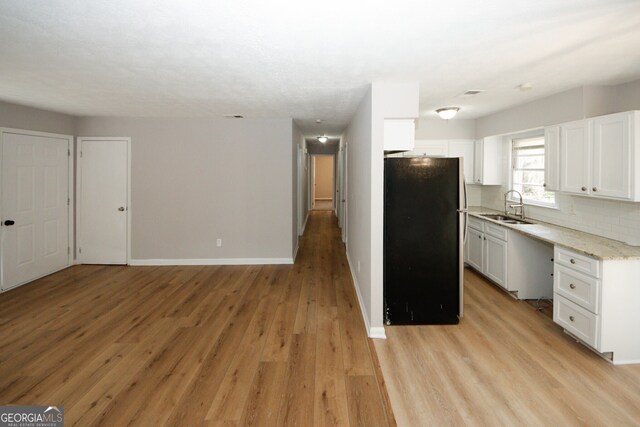 kitchen featuring black fridge, white cabinetry, sink, and light hardwood / wood-style flooring