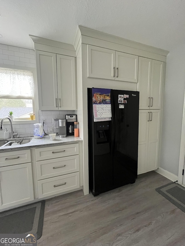 kitchen featuring decorative backsplash, light hardwood / wood-style floors, black fridge, and sink